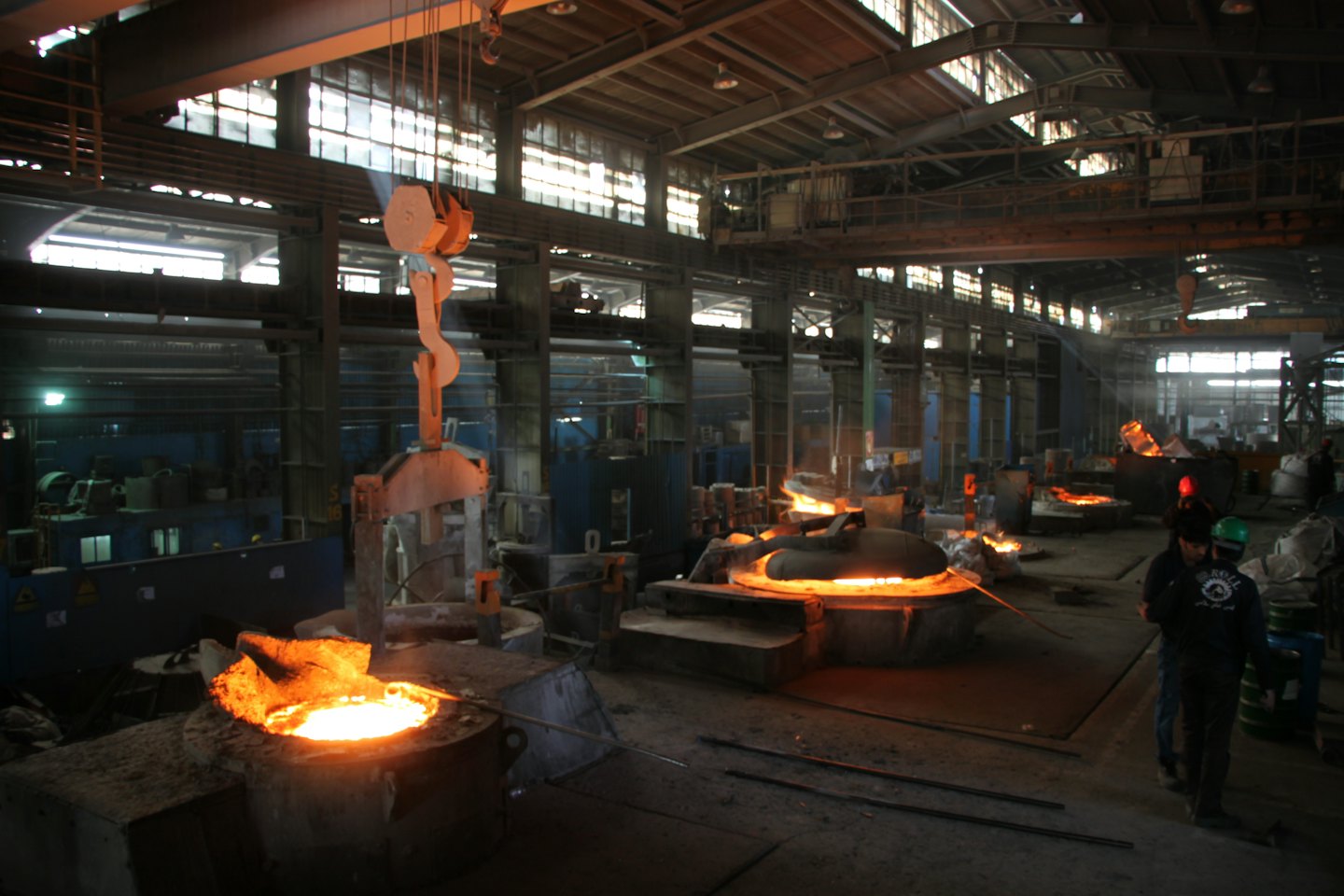 Two industrial workers monitor molten metal inside a factory foundry.