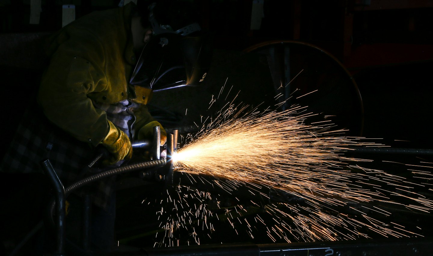 Metalworker in yellow jacket welding with bright sparks.