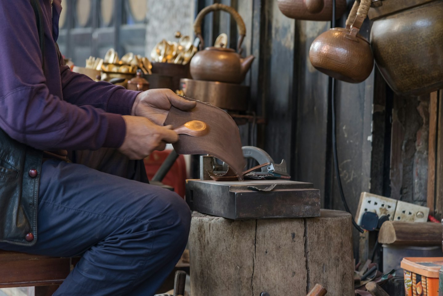 Craftsman shaping copper metal piece with a hand tool.