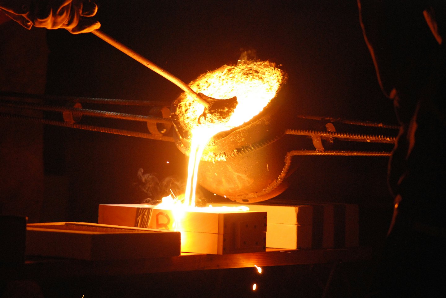 Gloved hands pour molten metal into rectangular foundry molds.