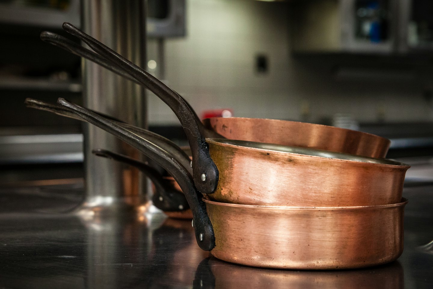 Copper pots with cast iron handles on a stainless steel counter.