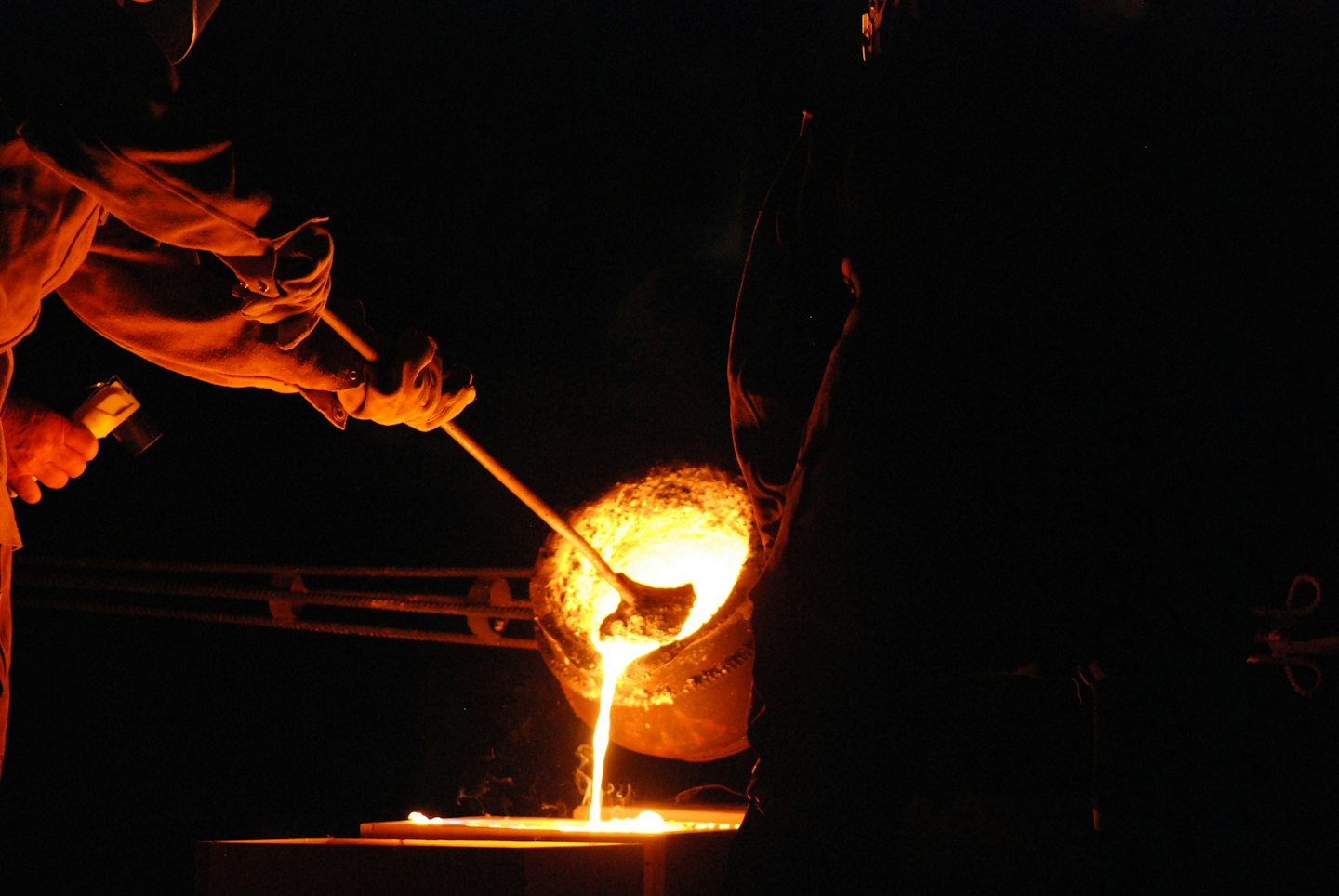 Workers pour glowing molten metal into a mold.
