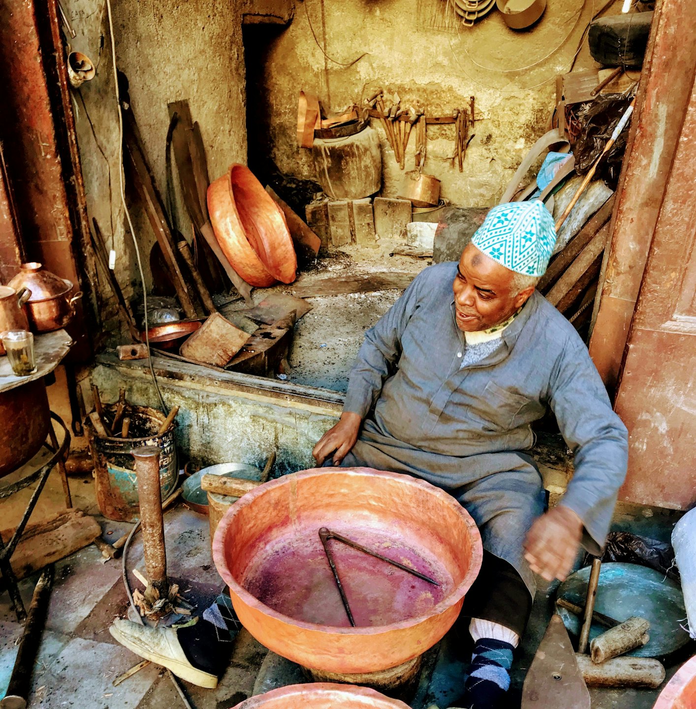 Coppersmith works on large copper vessels in a rustic outdoor workshop.